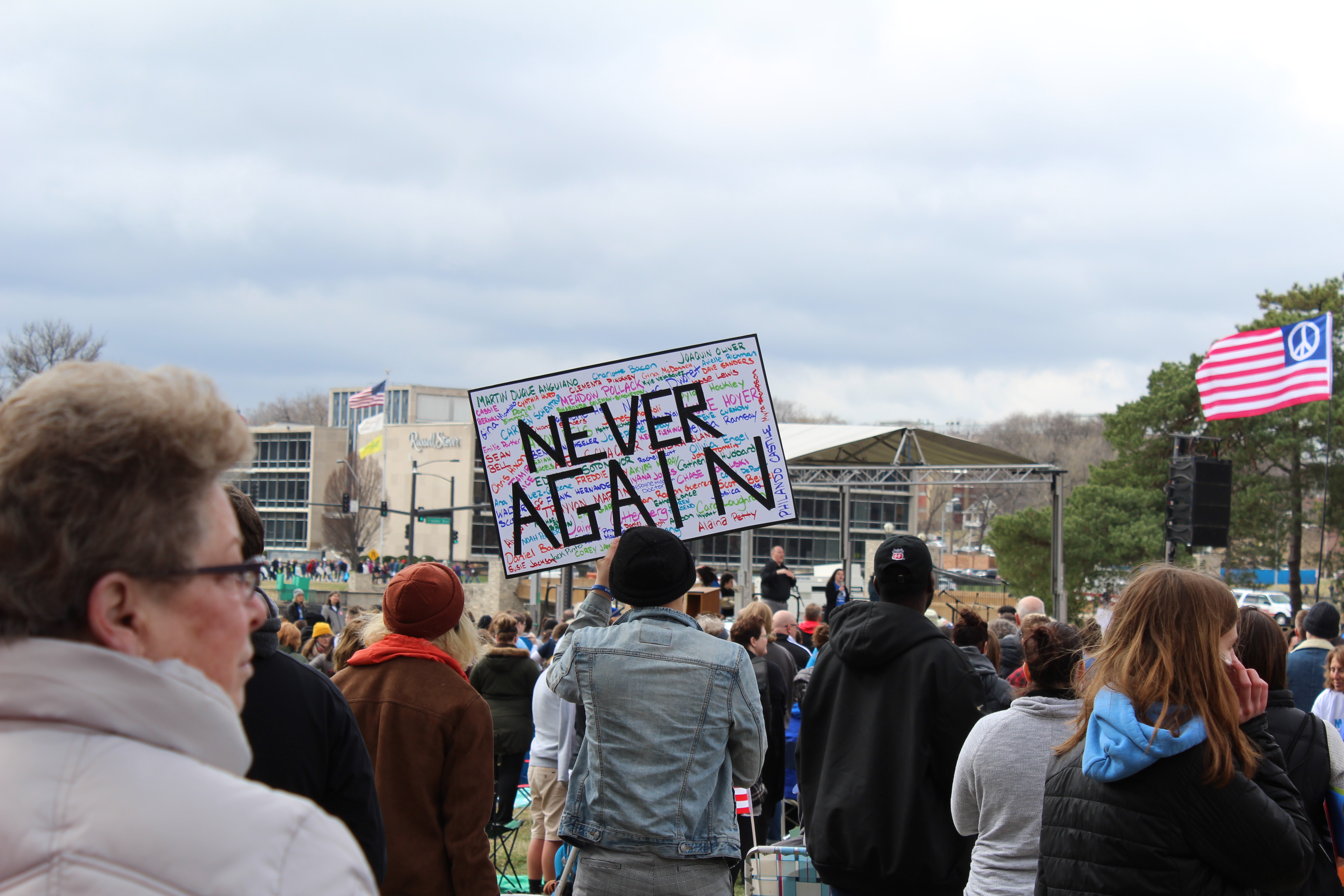A protester holds up a large sign during speaker presentations that includes the names of victims in multiple colors, with the contrast of black letters to say “Never Again.” The protester held the sign up while the crowd chanted “never again, never again,” after a speaker held a roll call for all those who had died in the Parkland, Florida shootings. Photo: Carina Smith, 14 East.