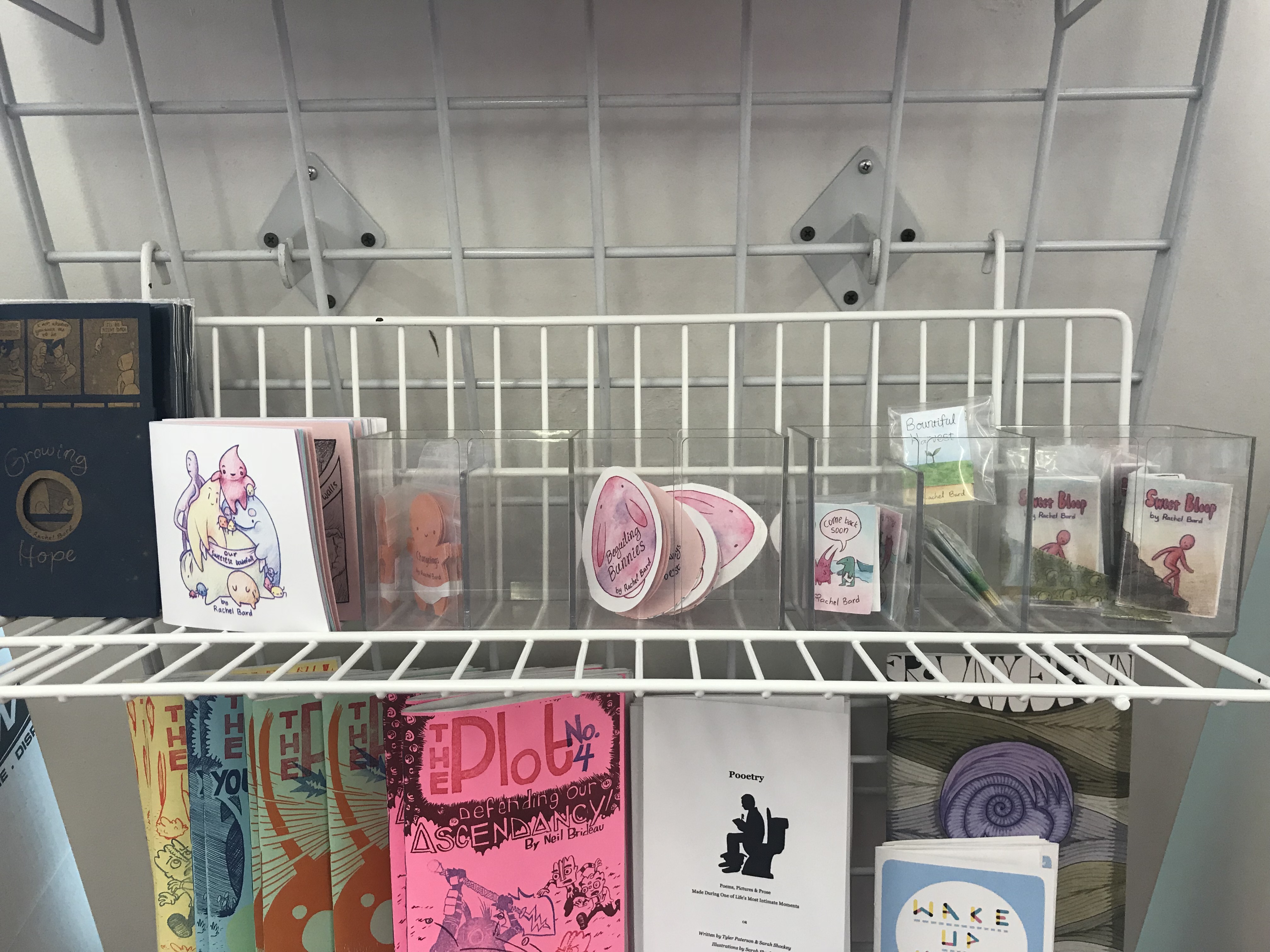 Small zines and comics from Rachel Bard on display. Most include cutesy drawings of rabbits, babies and other blobbish critters